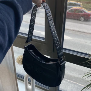 Svart väska från Nelly  - Svart handväska från Nelly med silvriga ” pärlor” på axelbandet. Den är väldigt stor och rymlig . Använd fåtal gånger men fortfarande i väldigt bra skick