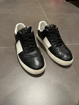 Svarta och vita sneakers från Valentino - Valentino flycrew. Skorna har svarta snören, vit sula och diskret logga på plösen samt under sulan. Klassisk låg modell med stilren design som passar till allt! Hör av er vid frågor. (En nit saknas)