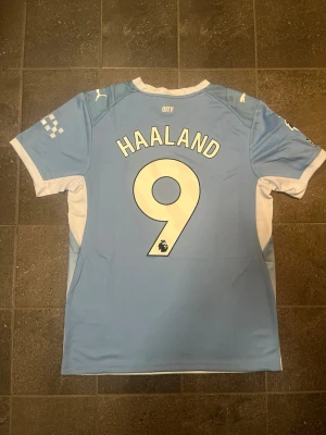 Manchester City Haaland #9 Match tröja - Snygg Manchester City matchtröja i ljusblått med vita detaljer. Erling Haaland #9 på ryggen. Tröjan har klubbmärke och Puma-logga på bröstet samt Etihad Airways som sponsortryck. Tillverkad i lätt och ventilerande funktionsmaterial, perfekt för fotboll eller träning.