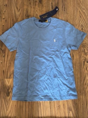 Blå t-shirt från Polo Ralph Lauren - Snygg ljusblå t-shirt från Polo Ralph Lauren med klassisk passform och det ikoniska broderade logotypen på bröstet. Tillverkad i mjuk bomull och har rund halsringning samt korta ärmar. Perfekt till jeans eller shorts.
