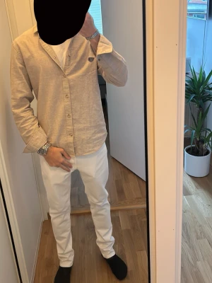 Beige jack and Jones  linneskjorta med knappar  - Säljer en stilren beige skjorta i linne med klassisk krage och knappar framtill. Skjortan har lång ärm och en avslappnad passform som passar perfekt till både jeans och chinos. Enkel och snygg design som funkar året runt.