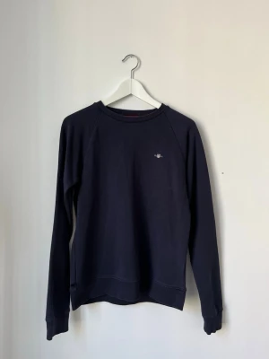 Mörkblå sweatshirt från GANT - Mörkblå sweatshirt från GANT i storlek 176, 16 år. Mycket bra skick förutom ett hål i tröjan på sidan- se bild 