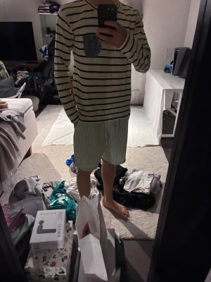 Randig långärmad tröja med ficka - Vit långärmad tröja med svarta horisontella ränder och en blå bröstficka med knapp. Tröjan har en avslappnad passform och rund halsringning. Perfekt för en casual och stilren look. Står XL men storleken är mer mot M/L-hållet. Storlek: M/L | Skick: 8,5/10 | Pris: 15€.