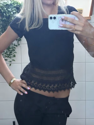 Svart topp med spetsdetaljer - Säljer en svart topp med korta ärmar och snygga spetsdetaljer nertill. Toppen har ett genombrutet parti och vågig spetskant som ger en trendig look. Perfekt att styla med både jeans och kjol.
