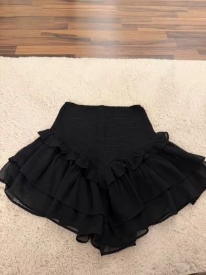 Svart volangkjol  - Supersöt svart kortkjol från Gina Tricot med bred smock i midjan och dubbla volanglager. Säljer då den inte kommer till användning💗 