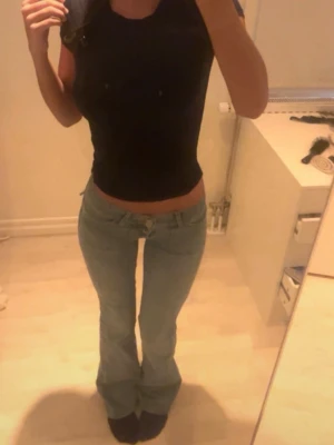 Ljusblå bootcut jeans med låg midja - Säljer ett par ljusblå jeans, låg midja.  Bakfickor med knapp, köpta från Nelly.