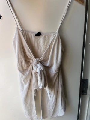 knyttröja - Säljer en ljusbeige strandklänning i mjukt frottéliknande material. Klänningen har smala axelband och en snygg knytning framtill som ger en avslappnad och trendig look. Perfekt att slänga på sig över bikinin på stranden.