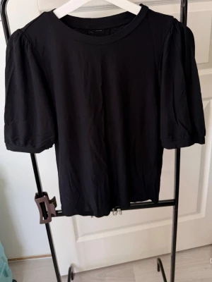 Svart topp med puffärm - En svart topp med puffiga kortärmar och rund halsringning. Tillverkad i mjukt material som känns bekvämt mot huden. Enkel och stilren design som passar till många olika looks.