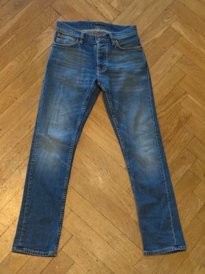 Nudie grim Tim faded memory  - Säljer ett par blå jeans med raka ben från nudie. Klassisk femficksmodell med normal midja och kontrastsömmar. Materialet är denim i bomull med lite stretch för extra komfort. Modellen är grim tin faded memory. Nypris är 1600kr, jag säljer för 600kr dem är använda två gånger och säljer för att dem är för stora. Skriv dm för frågor. Str w28 L30