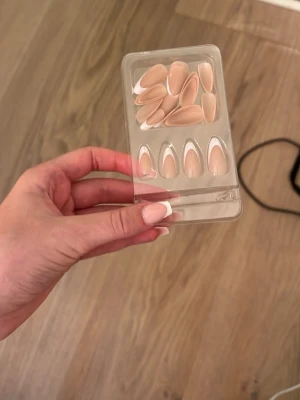 Nude franska press-on naglar - Säljer ett set press-on naglar i nude färg med vit fransk tipp. Naglarna har en elegant almondform och är tillverkade i plast. Perfekt för dig som vill ha snygga naglar snabbt och enkelt. Helt oanvända