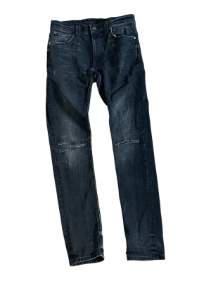 Nudie jeans slim jim - Säljer ett par svarta Nudies med modellen slim Jim med raka ben och slitningar på både fram- och baksida. Materialet är denim med en något tvättad finish.                                  Storlek: w:29 L:32                            Nypris ligger på 1600 och byxan är i nytt skick