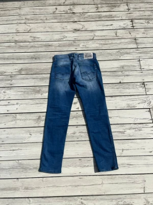 Blå jeans från Replay - Säljer ett par blå jeans från Replay med raka ben och klassisk femficksmodell. Jeansen har snygga slitningar och tvättade detaljer för en avslappnad look. Materialet är denim i bomull och passformen är normal. Perfekta till en casual stil.