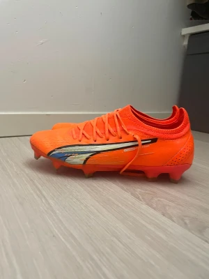 Puma Ultraweave elites - Säljer ett par grymma Puma Ultra fotbollsskor i en riktigt snygg orange färg med svart och silverdetaljer på sidan. Skorna har snörning, låg vikt och är tillverkade i syntetmaterial för bästa känsla på planen. Perfekta för dig som vill sticka ut och få max speed.