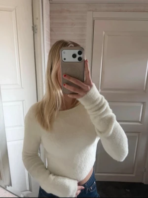 Vit fluffig cropped stickad tröja - Säljer en supermjuk och fluffig vit stickad tröja med croppad passform och långa ärmar. Tröjan har rund halsringning och är perfekt för dig som gillar en enkel men trendig look. Materialet känns mysigt och passar till många olika outfits.