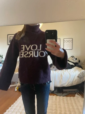 Mörklila stickad tröja med text - Mysig mörklila stickad tröja med hög krage och breda ärmar. På bröstet står det 'LOVE YOURSELF' i vit text. Perfekt för kalla dagar och ger en cool vibe till din outfit.