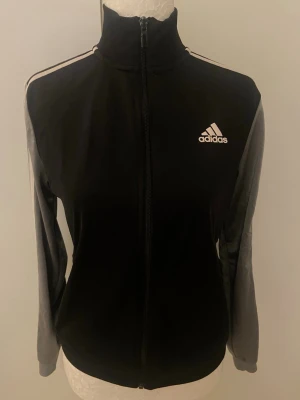 Svart Adidas kofta - Svart/grå kofta från Adidas med vit logga. Använd några gånger. Tror att storleken är S (har ej lappen kvar). 