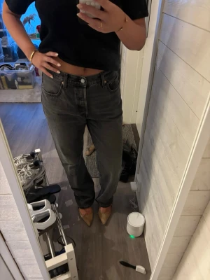 Svarta raka jeans med mid midja LEVIS - Säljer ett par svarta raka jeans med hög midja och klassisk femficksmodell. Jeansen har en avslappnad passform och är perfekta för en trendig och enkel look. Materialet är kraftigt denim i bomull och färgen är tvättad svart. Använt fåtal gånger