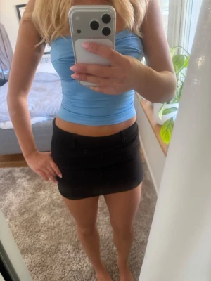 Svart kortkjol i bomull - Säljer en svart, tight kortkjol i bomull med minimalistisk design. Kjolen har bälteshällor och två dekorativa fickor framtill. Perfekt att matcha med crop tops eller oversized tröjor för en trendig look.