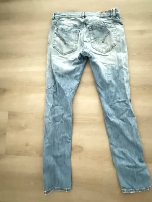 Ljusblå slitna jeans med smal passform - Säljer ett par ljusblå jeans med smal passform och slitningar på vänster lår. Jeansen har klassiska fem fickor och är tillverkade i denim. Perfekta för en avslappnad och trendig look.