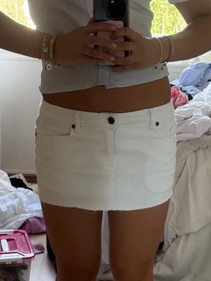 Vit miniskirt - Snygg vit kort jeanskjol med rå kant nertill och klassiska fickor fram och bak. Kjolen har knapp och dragkedja framtill samt bälteshällor. Den är väldigt kort, lågmidjad och jag har klippt själv