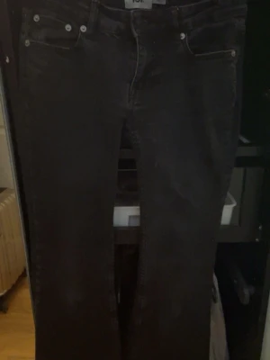Svarta bootcut jeans med fem fickor - Säljer ett par svarta jeans med klassisk femficksmodell och bootcut passform. Jeansen har silverfärgade nitar och knappdetaljer samt subtila slitningar baktill. Perfekta för dig som gillar en tidlös och avslappnad stil. Lite slitet på rumpan och några små små fläckar bak på låret.