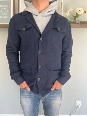 Brunelli Skjortjacka Marinblå S 37/38 - Brunelli overshirt/skjortjacka i marinblå med klassisk krage, knappstängning fram, axelklaffar med knapp och två stora bröst/mag-fickor. Snygg detaljerad design med militärinspirerade drag.  Skick: bra skick, inga hål eller fläckar Storlek: S (37/38) Modell: 175 cm / 65 kg — sitter true to size på bild