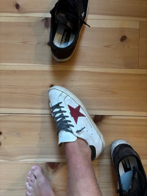 golden goose  - Snygga vita sneakers med en röd stjärna på sidan, grå skosnören och grön detalj på hälen. Klassisk låg modell med slitna detaljer för en trendig look. Perfekta för dig som gillar streetstyle och vill sticka ut lite extra.