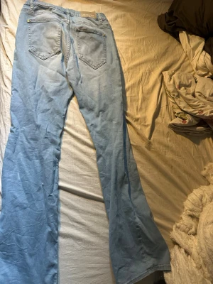 Ljusblå utsvängda jeans från Lindex - Säljer ett par ljusblå jeans från Lindex med utsvängda ben och klassisk femficksmodell. Jeansen har hyfsat lågmidja och är tillverkade i ett mjukt denimtyg som ger en skön och avslappnad look.
