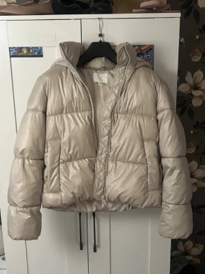 Ljus pufferjacka - Säljer en beige pufferjacka med dragkedja och stor huva. Jackan sitter fint, perfekt för kalla dagar och enkel att matcha med olika outfits. Materialet är glansigt och ger en modern vibe. Det är storlek xs men skulle också säga att den passar som S då den är ganska stor, men det beror såklart på vad man gillar. Längden är jättebra, går ner lite över rumpisen. Säljer den då jag har för många jackor. Den har haft sminkfläckar i kragen men de syns inte längre då jag tvättat bort det, men bild finns