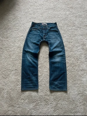 Levis 506 standard - Säljer ett par blåa bootcut/straight jeans med bred passform och raka ben. Jeansen har klassisk femficksdesign och tydliga sömmar. Materialet är denim i 100% bomull och färgen är mellanblå med lätt slitning. Perfekta för en avslappnad och trendig stil. 😴Priset är ej hugget i sten så kom gärna med förslag!🙂