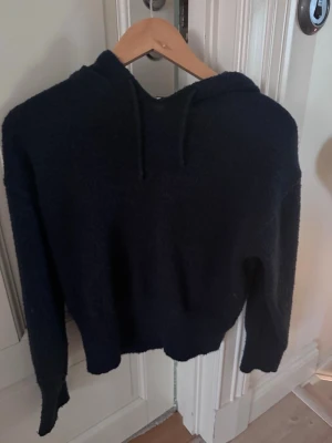 Mörkblå stickad hoodie med huva - Mysig mörkblå stickad hoodie med huva och dragsko. Tillverkad i ett stickat, mjukt material som ger en avslappnad och trendig look. Långärmad modell med ribbade muddar vid ärmslut och nederkant. Perfekt för dig som gillar en chill och enkel stil.