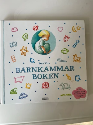 Den vita Barnkammarboken - En färgglad och illustrerad barnbok med titeln 'Den vita Barnkammarboken' från Bonnier Carlsen. Boken har hårda pärmar och innehåller ramsor och sånger, samt en medföljande CD. Omslaget pryds av lekfulla illustrationer i olika färger.