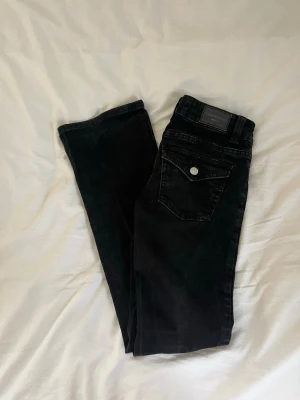 Svarta jeans - Svarta low wasted bootcut jeans från Gina med knappar på bakfickorna! Sköna och fina