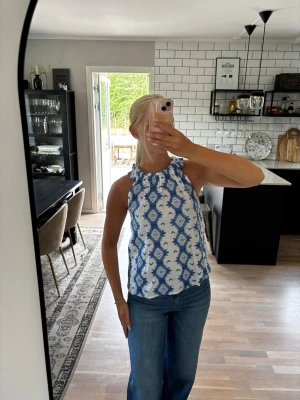 Blåvit mönstrad ärmlös topp - Säljer en superfin ärmlös topp med blått och vitt  mönster. Använd 1 gång så toppen är i nyskick. Publicerad på flera säljsidor 🌸