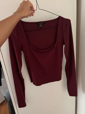 Vinröd långärmad topp med djup ringning - Säljer en vinröd långärmad topp från Aimiu med djup, rundad ringning. Toppen har en slim passform och är tillverkad i ett mjukt, stretchigt material som sitter snyggt på kroppen. Perfekt att styla med jeans eller kjol.