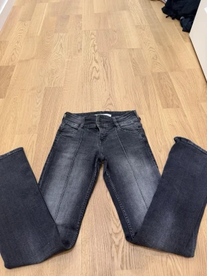 Grå bootcut jeans med pressveck - Säljer ett par grå bootcut jeans med markerade pressveck framtill. Jeansen har klassisk femficksmodell, normal midja och lätt utsvängda ben. Materialet är stretchigt denim som ger en bekväm passform. Perfekta för en trendig och avslappnad look.
