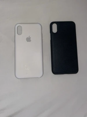 Två mobilskal till iPhone X/XS - Säljer två mobilskal till iPhone X/XS. Ett är vitt med Apple-logga i silikon och det andra är svart med räfflad yta för extra grepp. Båda har öppning för dubbel kamera och är tunna och smidiga att använda.
