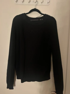 Svart stickad tröja Black Label M - Snygg svart stickad tröja från The Black Label Collection i storlek M. Tröjan har rund halsringning, långa ärmar och en klassisk rak passform. Perfekt att matcha med jeans eller kjol för en stilren look.