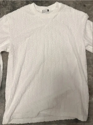 Vitt set med strukturmönster - Säljer ett vitt set bestående av långärmad tröja och shorts. Båda plaggen har ett diskret strukturmönster i tyget och tröjan har rund halsringning. Shortsen har resårmidja med dragsko och sidofickor. Perfekt för dig som gillar stilrena och bekväma plagg.