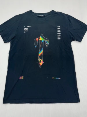 Svart Trapstar t-shirt ”ITS A SECRET” - Beskrivning  Säljer en svart T-shirt från Trapstar. Storlek M. Bra skick. Trycket är sprucket/slitet – jag är osäker på om det är originaldesignen eller slitage, så bilderna får avgöra. Färgglatt motiv framtill och texten "IT'S A SECRET" nedtill. Exklusiv tröja.  • Skick: Bra skick (trycket är sprucket, osäker på om det ska vara så) • Storlek: M • Färg: Svart • Märke: Trapstar • Typ: T-shirt.                    Hör av dig vid frågor eller liknande!