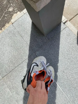 Vita och orangea Nike fotbollsskor - Säljer ett par vita Nike tiempo elite version fotbollskor med svarta detaljer och orange insida. Skorna har snörning och är designade för bra grepp på planen. Perfekta för dig som vill ha stilrena och funktionella skor till match eller träning. Jätte eleganta skor som är suveräna man känner av verkligen känslan med bollen med denna skor.