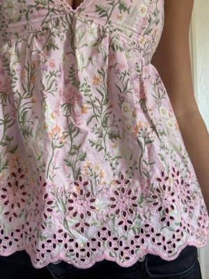 Blommig rosa linnetopp med spets - Söt rosa linnetopp med blommigt mönster och broderad spetskant nertill. Toppen har smala axelband, v-ringning och en luftig passform. 