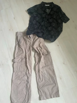 Beiga cargobyxor med fickor - Säljer ett par beiga cargobyxor med flera stora sidofickor och raka ben. Byxorna har klassisk cargostil och är perfekta för en avslappnad och trendig look. Materialet ser ut att vara bomull eller bomullsblandning.