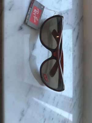 Bruna Ray-Ban solglasögon - Snygga solglasögon från Ray-Ban i brun plast med stora, rundade bågar och mörka linser. Klassisk och tidlös design som passar till de flesta outfits. Perfekta för soliga dagar och ger en cool vibe.