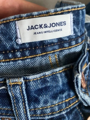 Blå raka jeans från Jack & Jones - Säljer ett par klassiska blå jeans från Jack & Jones med raka ben och snygga kontrastsömmar. Jeansen har fem fickor och är tillverkade i slitstarkt denimtyg. Perfekta för en avslappnad och trendig look.