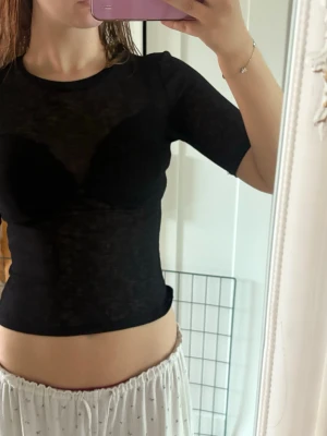 Svart mesh topp med kort ärm - Säljer en svart, tight mesh topp med korta ärmar. Toppen är genomskinlig och har en rund halsringning. Perfekt för att styla lager på lager eller för en trendig look.