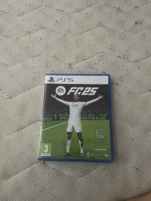 EA Sports FC 25 till PS5 - Säljer spelet EA Sports FC 25 till PlayStation 5. Omslaget är blått och spelet har en fotbollsspelare i vitt på framsidan. Inuti fodralet finns både skiva och manual. Perfekt för dig som gillar fotbollsspel och vill ha senaste versionen.