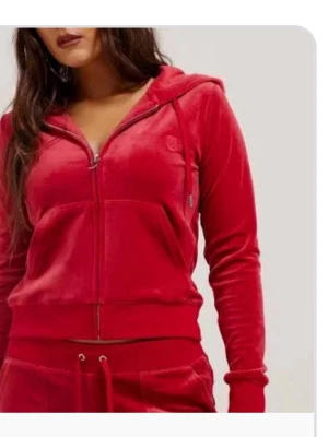 Juicy zip - Mysig röd hoodie i mjuk velour med dragkedja framtill och huva. Tröjan har fickor på sidorna och ribbade muddar vid ärmslut och nederkant. Perfekt för chill dagar hemma eller när du vill vara extra bekväm.