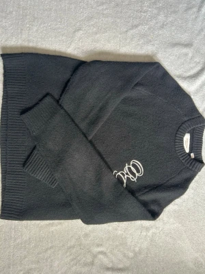 Svart stickad tröja Jack & Jones - Svart stickad tröja från Jack & Jones med rund halsringning och ribbade muddar vid ärmslut och nederkant. Tröjan har en diskret broderad textdetalj på bröstet och är perfekt för lager på lager under kyliga dagar. Orginalpris - 550kr 