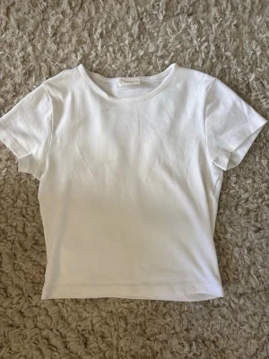 Vit basic t-shirt i bomull - Enkel och stilren vit t-shirt med rund hals och korta ärmar. Tillverkad i mjuk bomull för en bekväm känsla. Perfekt att matcha med jeans eller kjol för en clean look.